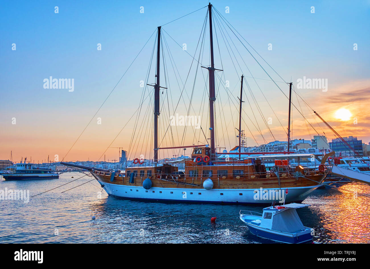 The seaside promenade is the best place to watch the sunset in Sliema, local sail yachts and ships look great in dimmed lights of evening sky, Malta Stock Photo