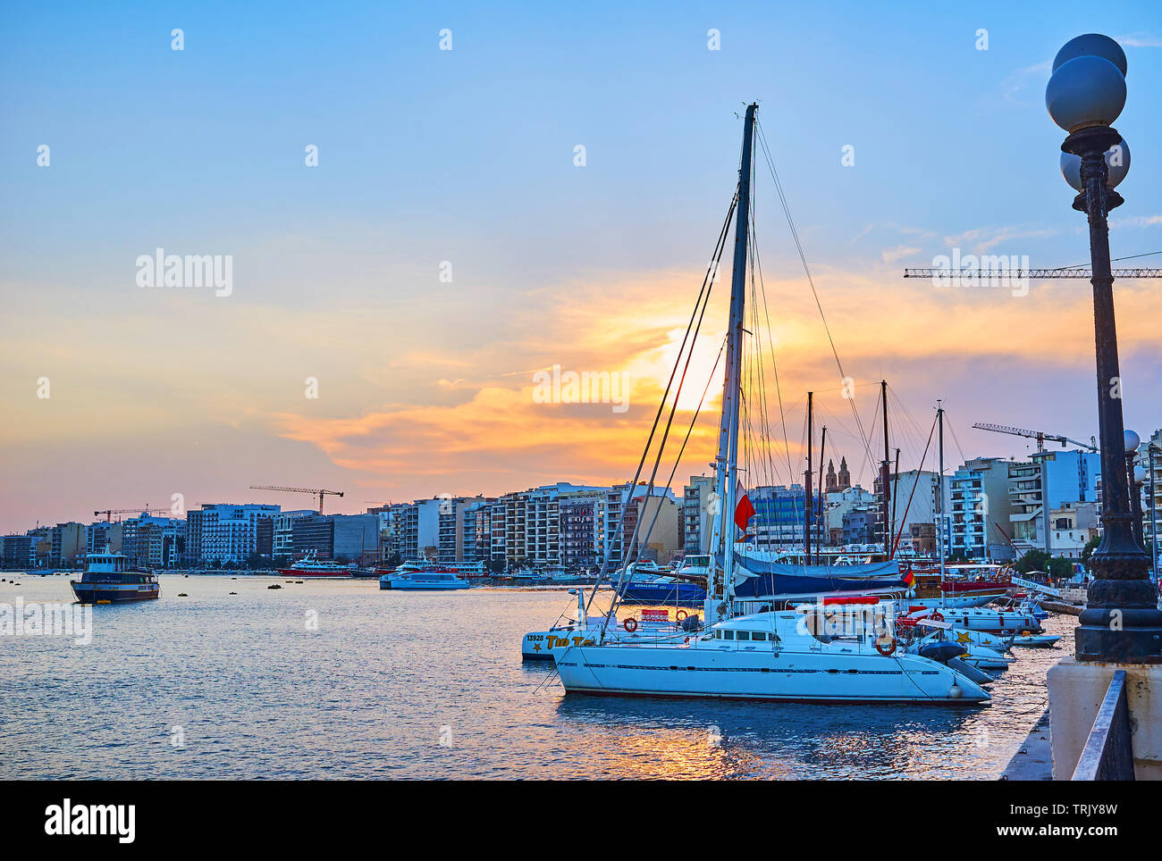 SLIEMA, MALTA - JUNE 19, 2018: The evening walk along the Sliema waterfront with a view on line of modern buildings, sail yachts and the bright sunset Stock Photo
