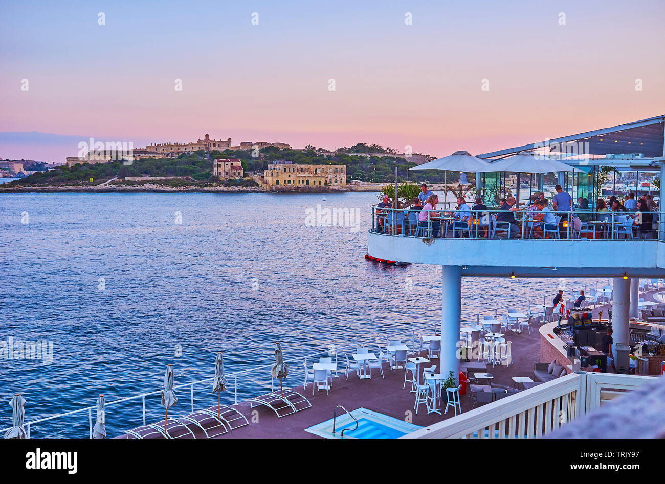 SLIEMA, MALTA - JUNE 19, 2018: The crowded open air terrace of the coastal restaurant on Tigne Point peninsula with a view on Valletta Northern Harbor Stock Photo