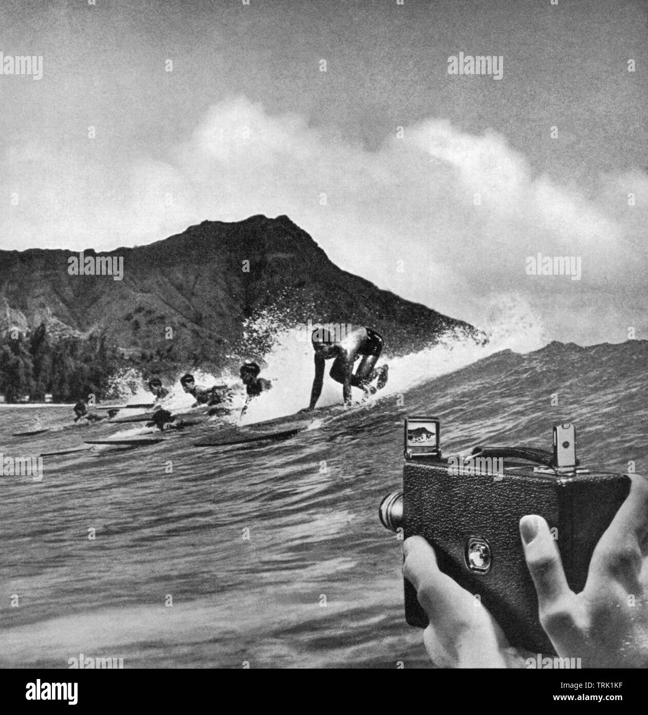 View of surfers catching a wave in Waikiki in a 1934 magazine ad for Kodak movie cameras. Stock Photo