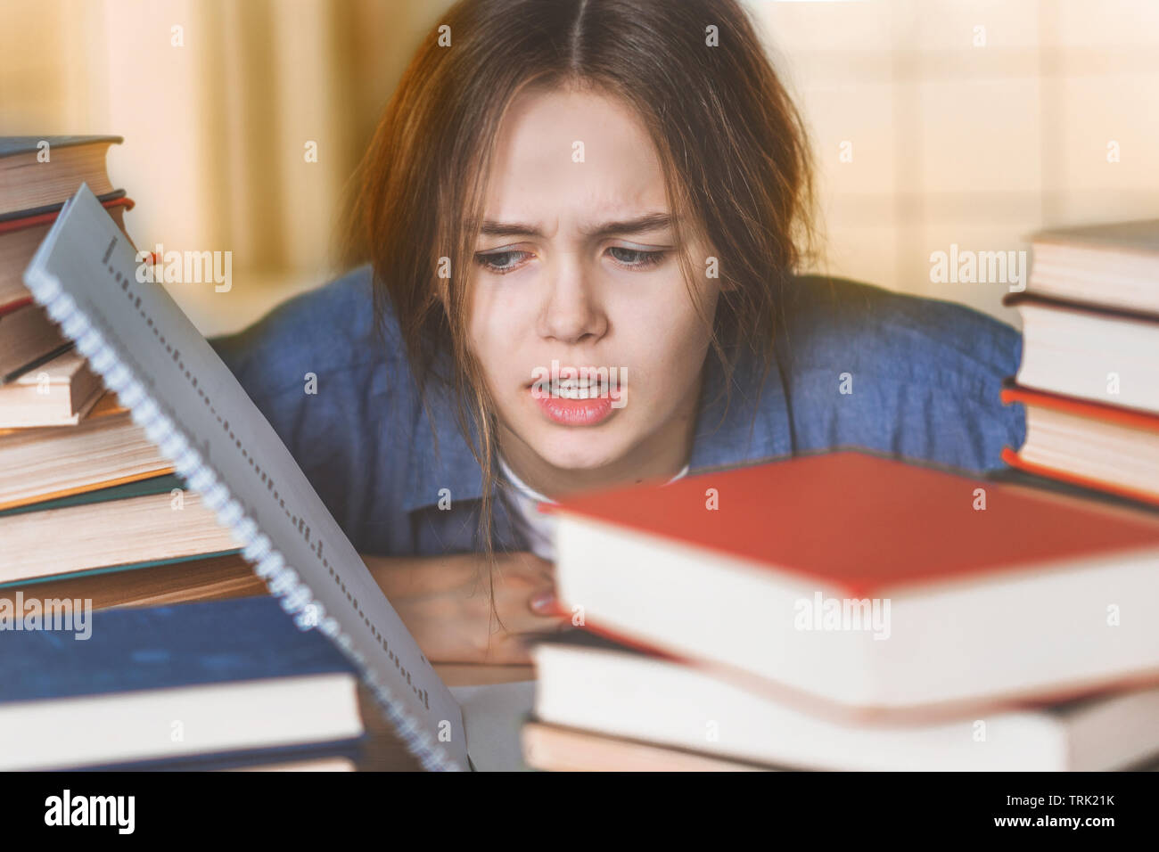 Upset woman sitting with closed eyes among textbooks and laptop, holding head in hands, annoyed by learning, feeling fatigue and despair, preparing fo Stock Photo