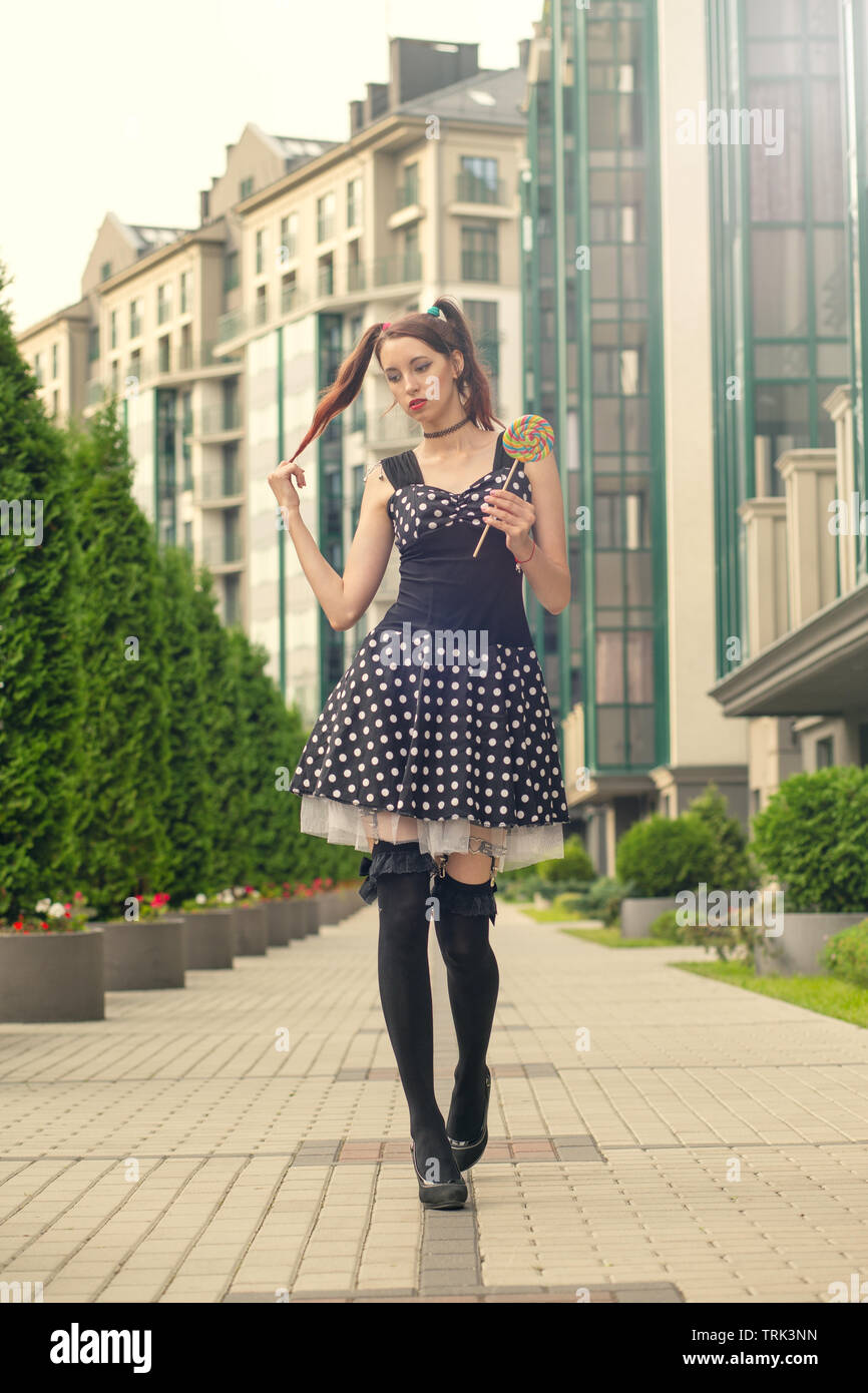 attractive young woman with candy in black dress walking on street ...