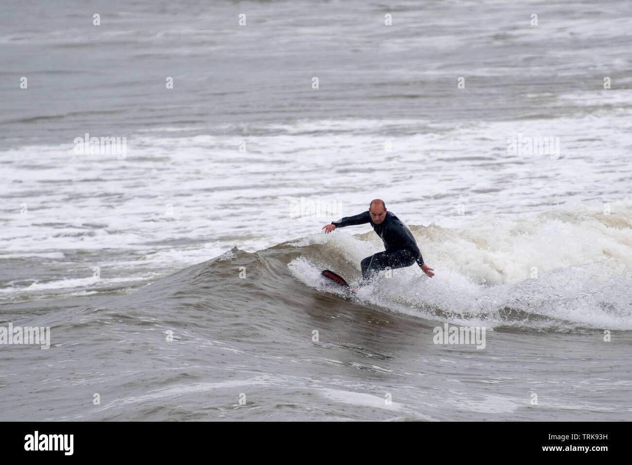 Even a bit of rain doesn't stop a middle-aged surfer from enjoying himself. Test Bay Porthcawl, UK. Stock Photo