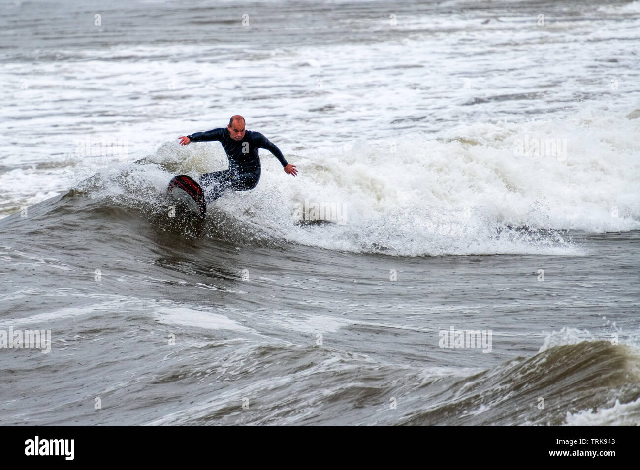 A middle-aged surfer riding the waves in the rain. Rest Bay, Porthcawl, UK. Stock Photo