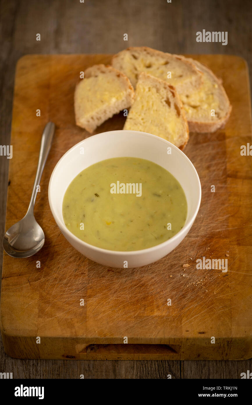 Fresh leek and potato soup in a bowl on a wooden board with crusty white bread and butter Stock Photo