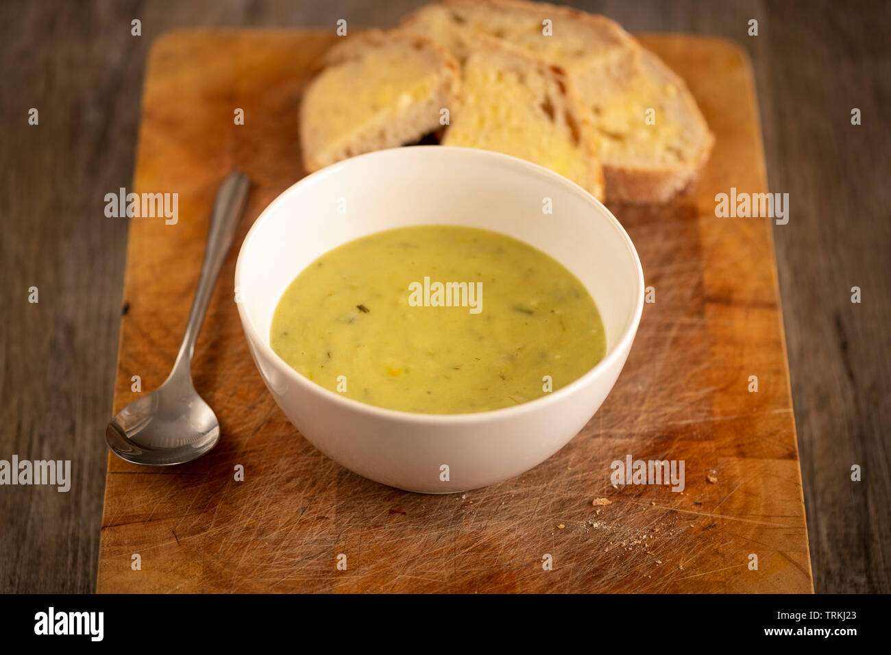 Fresh leek and potato soup in a bowl on a wooden board with crusty white bread and butter Stock Photo