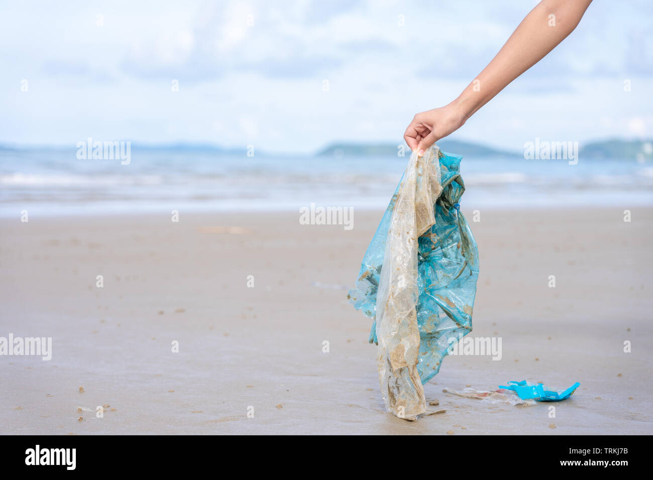 Woman’s hand picking up used plastic bag on sand beach, cleaning