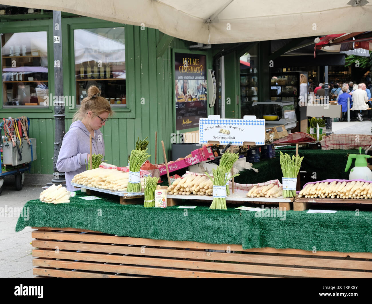 May 2019 - A young, caucasian blonde female sells white asparagus from a stand in the Victuals Market in Munich, Germany Stock Photo