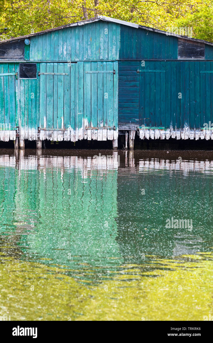 Shabby green wooden boat house shed is mirrored in water (copy space) Stock Photo