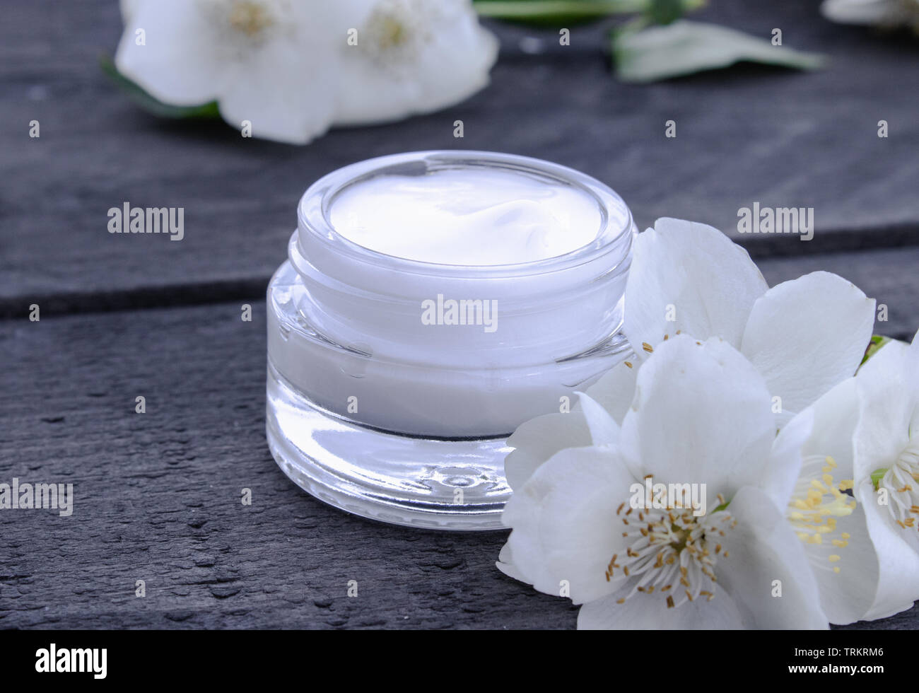 Cosmetic cream in a glass jar with jasmine flowers on a wooden background. Moisturizing face cream. Stock Photo