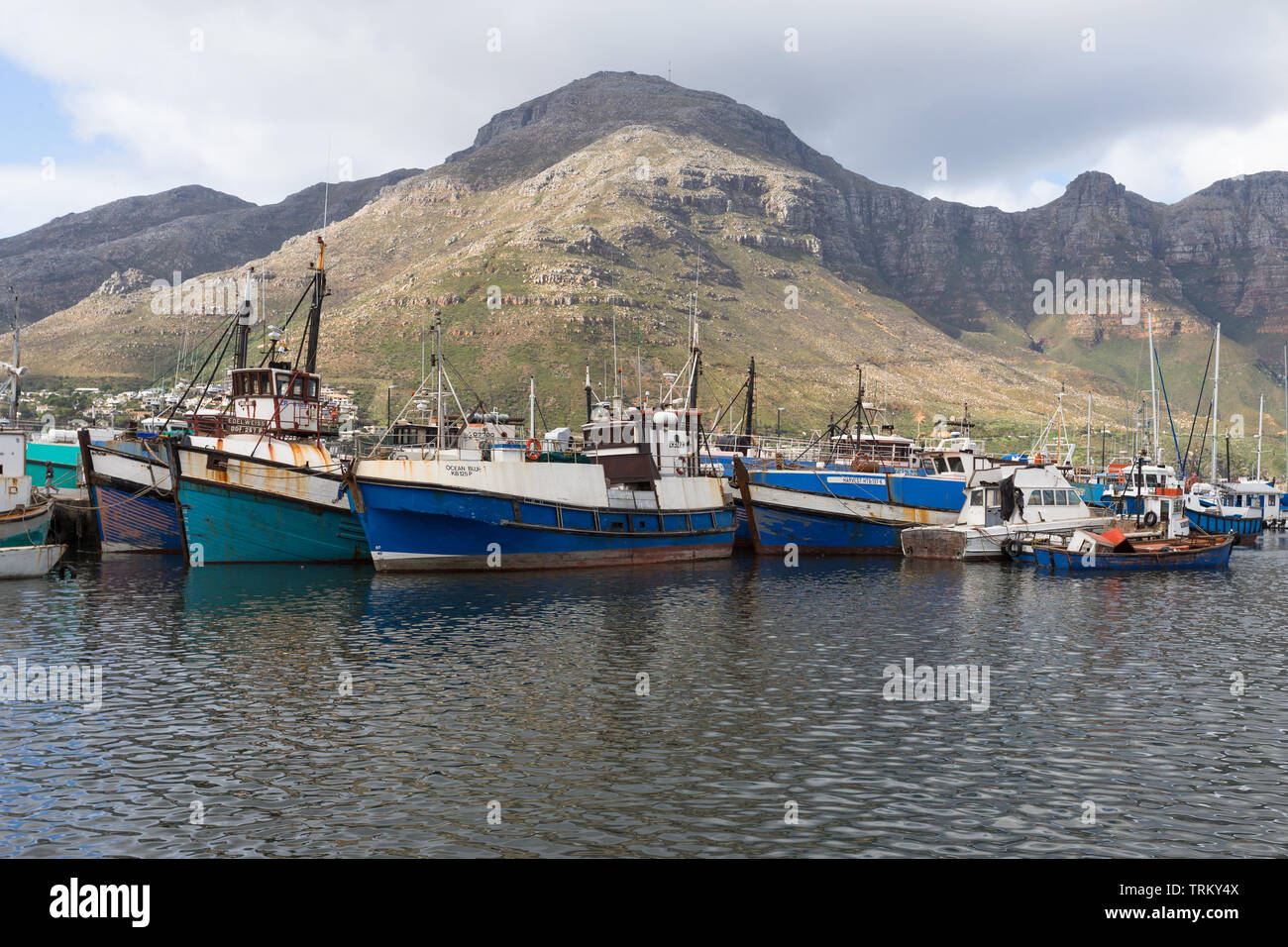 Hout Bay harbour and colourful commercial fishing boats or vessels against a backdrop of mountains in Cape Town, South Africa Stock Photo