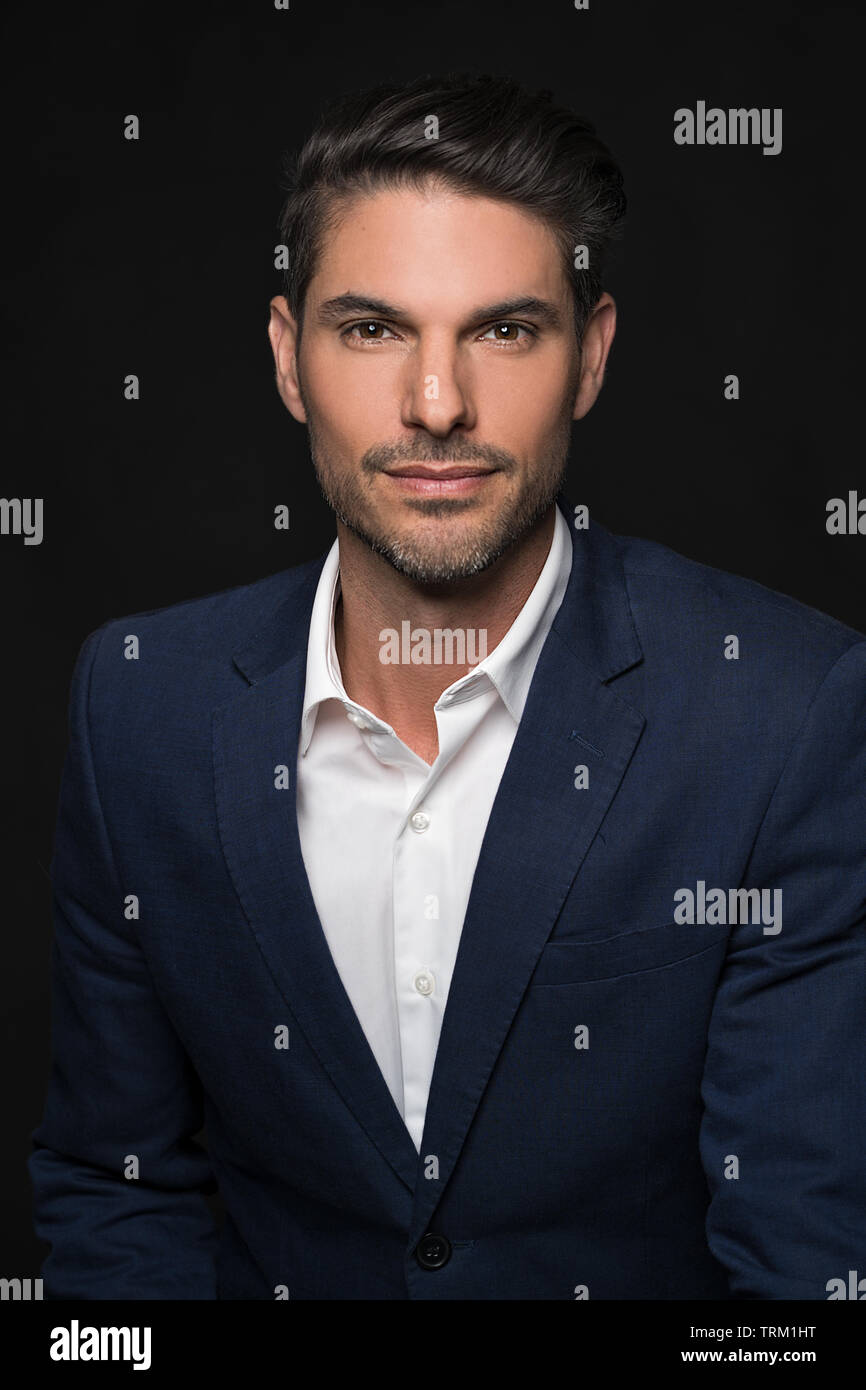 A good looking white male model modeling in a business suit, a half portrait, dark black background. He looks confident and handsome. Stock Photo
