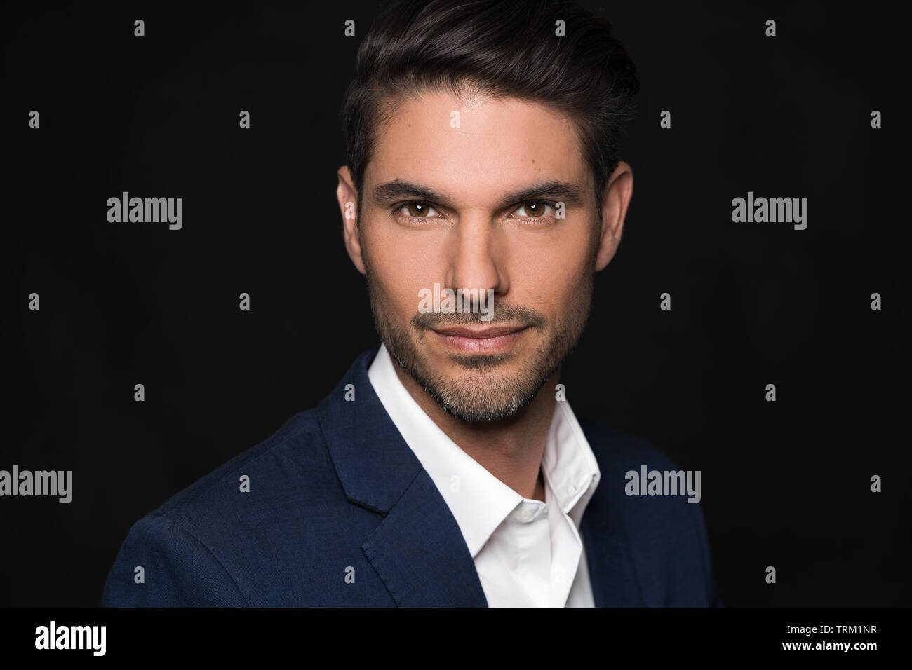 A good looking white male model modeling in a business suit, a head and shoulder portrait, dark black background. He looks confident. Stock Photo