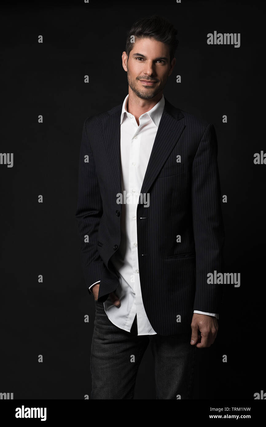 A good looking white male model modeling in a business suit, a three quarter portrait, dark black background. He looks happy, one hand in pocket. Stock Photo