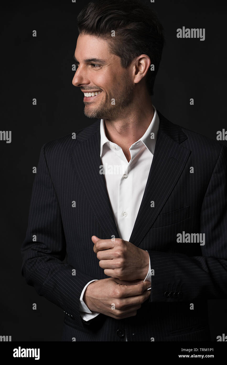 A good looking white male model modeling in a business suit, a half portrait, dark black background. He is smiling and looking away to the side. Stock Photo