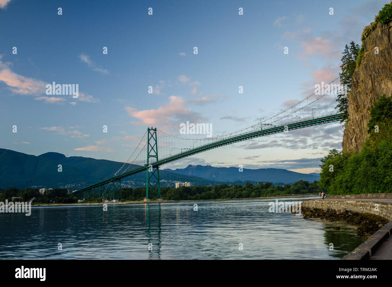 View of Lions Gate bridge from the seawall at the foot of steep cliff in Stanley Park, Vancouver, Canada. Stock Photo