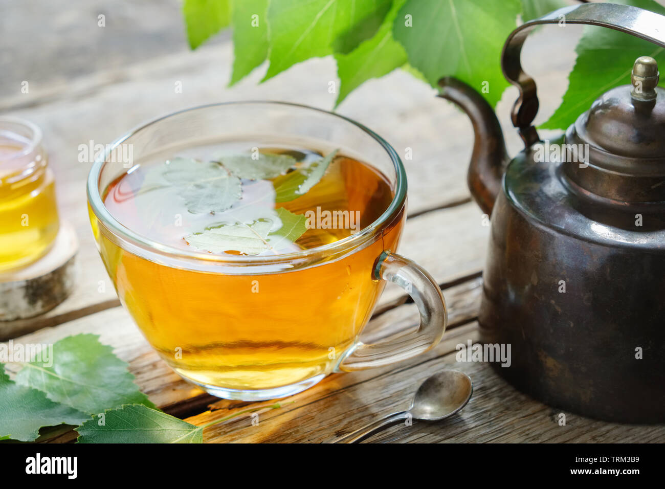 Birch leaves, healthy herbal tea cup, honey jar and vintage copper tea kettle. Stock Photo