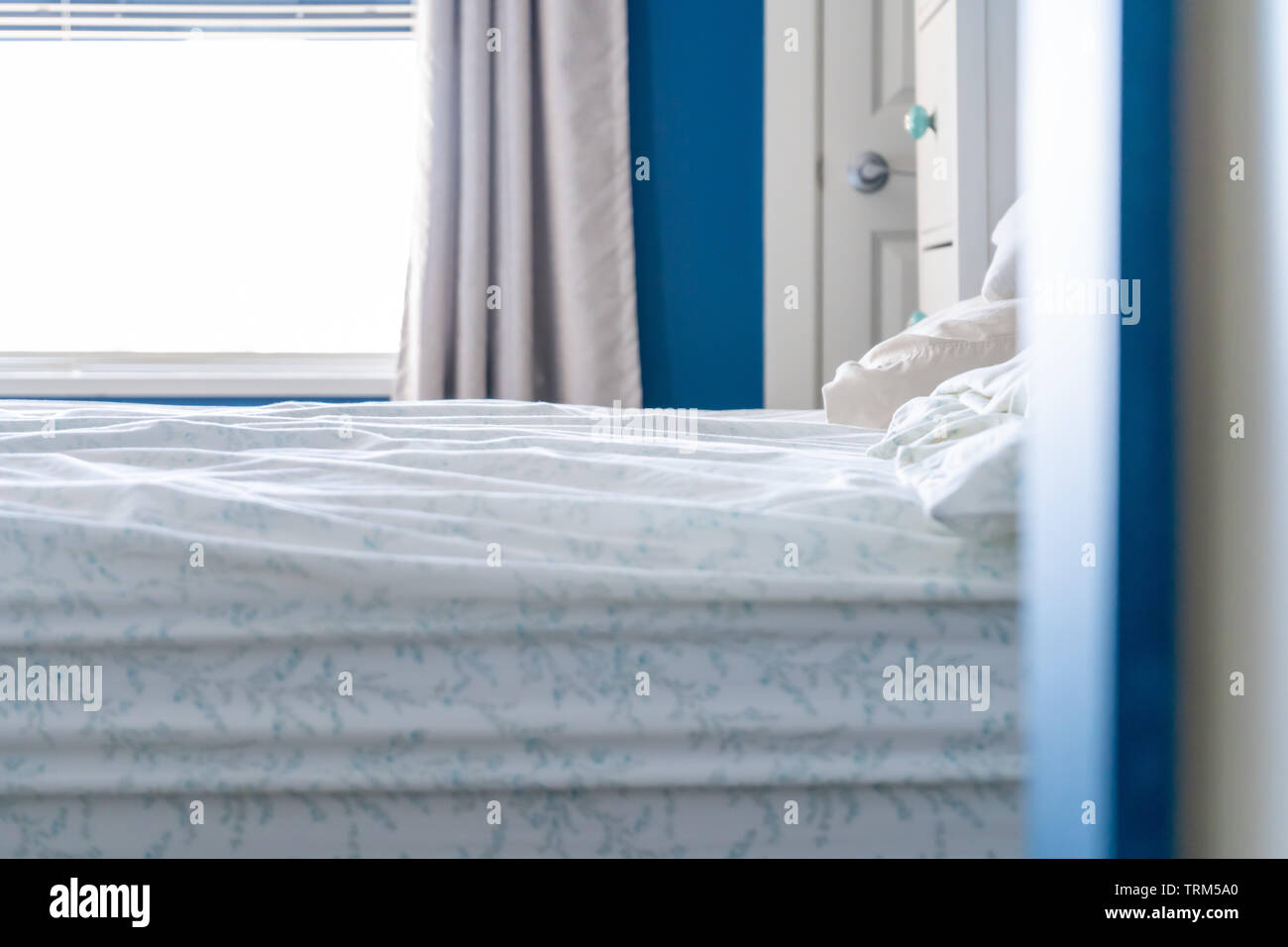 Low angle view of a slept-in bed with a messy sheet, no blankets, in a blue and white bedroom home design. Stock Photo