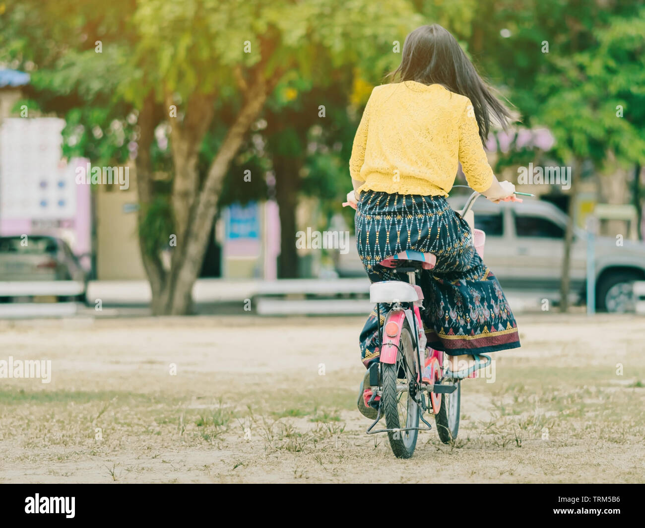 Back view of female teacher rides bicycle to teach students at ...