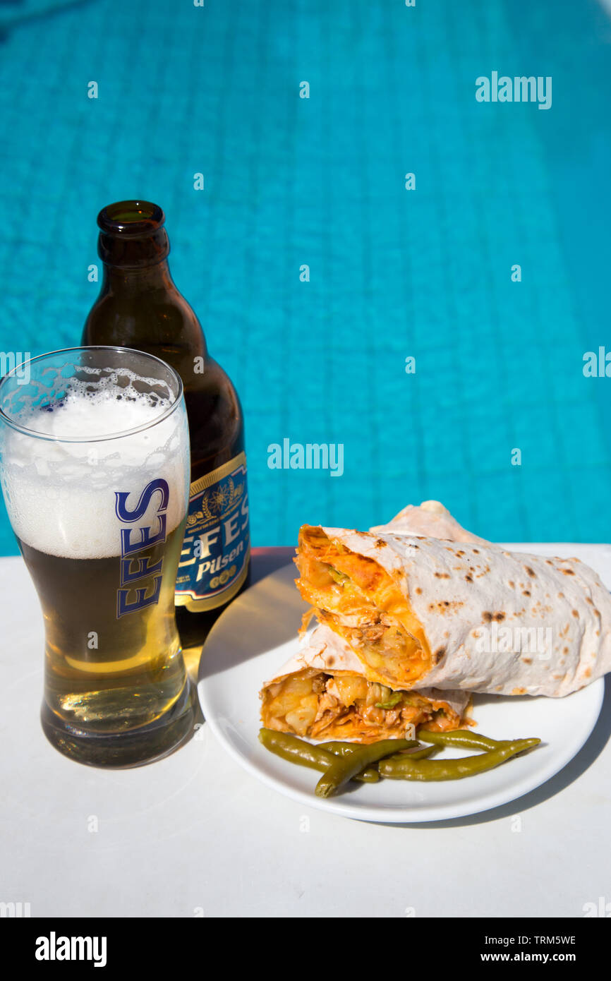 A plate of Turkish chicken kebab (Tavuk durum} served with a cold bottle of Efes pilsen beer on a sunny afternoon by the pool, Marmaris, Turkey Stock Photo