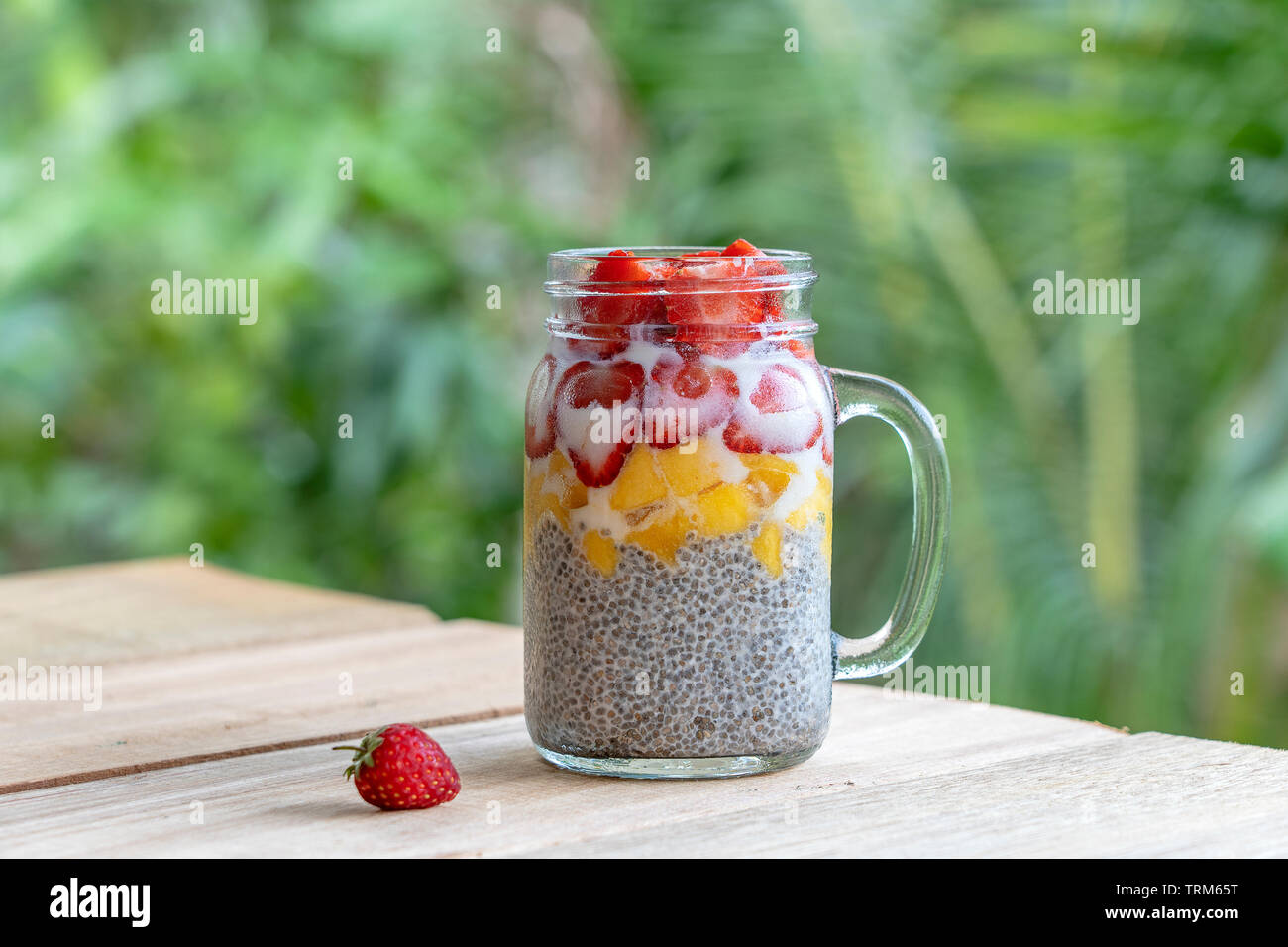 Almond milk chia pudding with fresh strawberries and mango in a glass jar mug. Vegan raw breakfast. Chia seeds and fresh cut fruits and berries desser Stock Photo