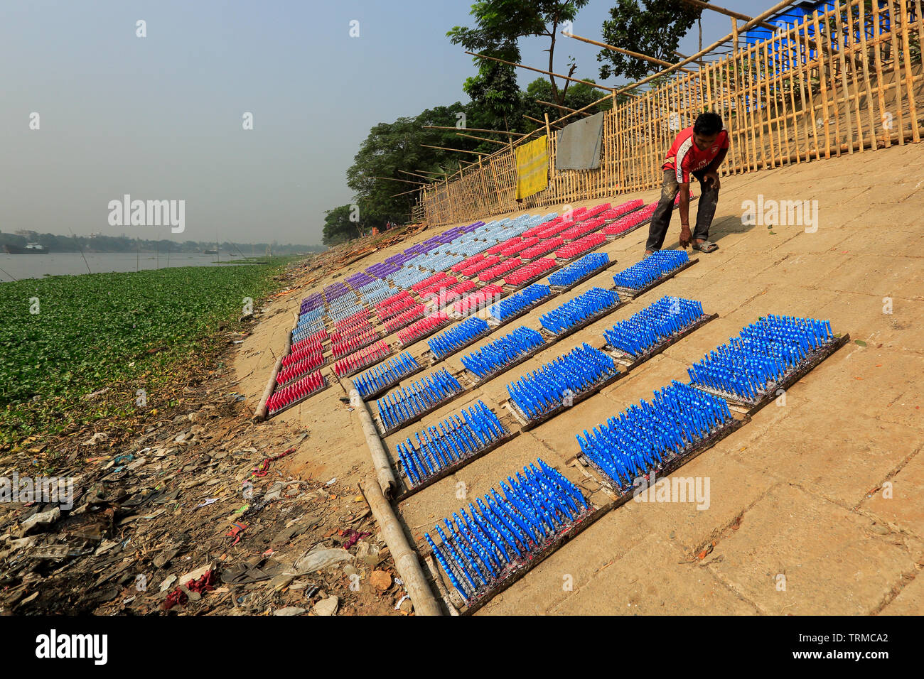 A laborer dries racks of rubber balloon in the sun as he works at a balloon factory in Dhaka, Bangladesh. Stock Photo