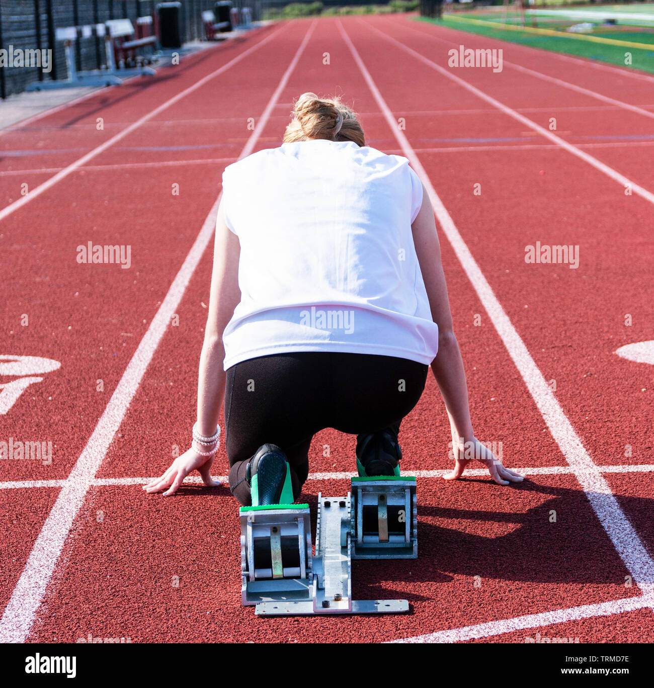 The view from behind the starting blocks of a high school female sprinter ready to run down the track at practice. Stock Photo