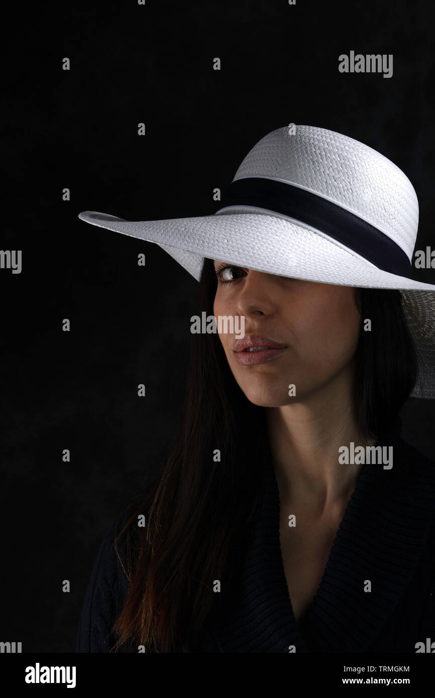 portrait of a beautiful young girl with a white hat on a black background,  looking at the camera Stock Photo