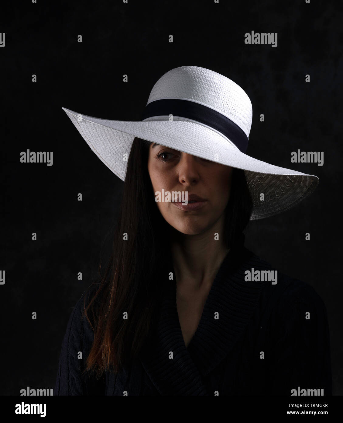 portrait of a beautiful young girl with a white hat on a black background, looking at her side Stock Photo