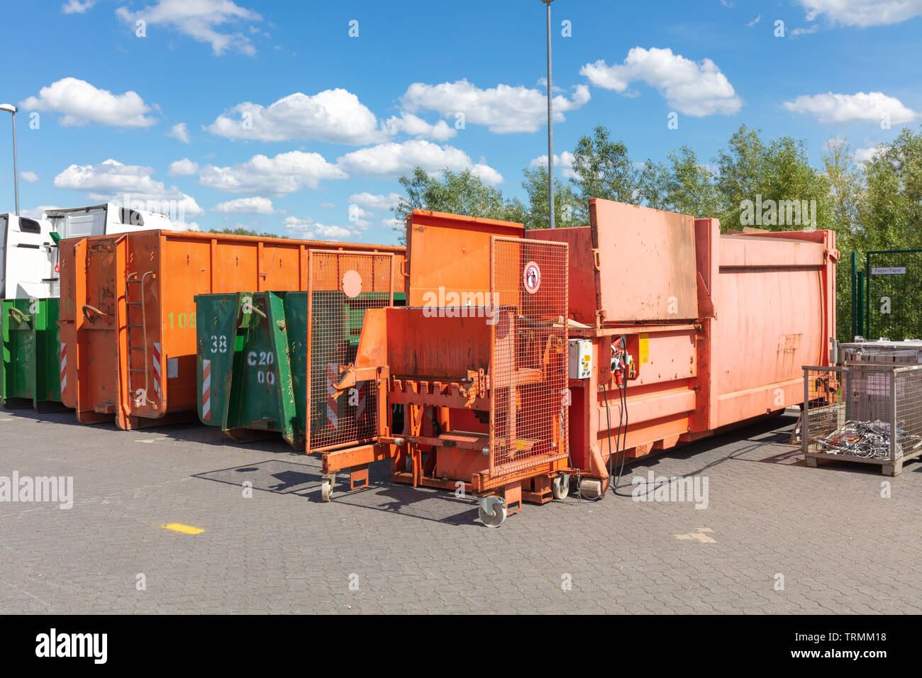 orange waste compactors are standing on a factory site with other waste