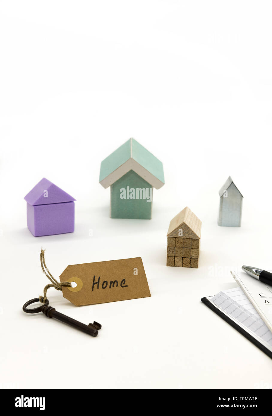 An old key with a sign on which is written "Home". Various model houses, an agenda, plans and a pen. Stock Photo