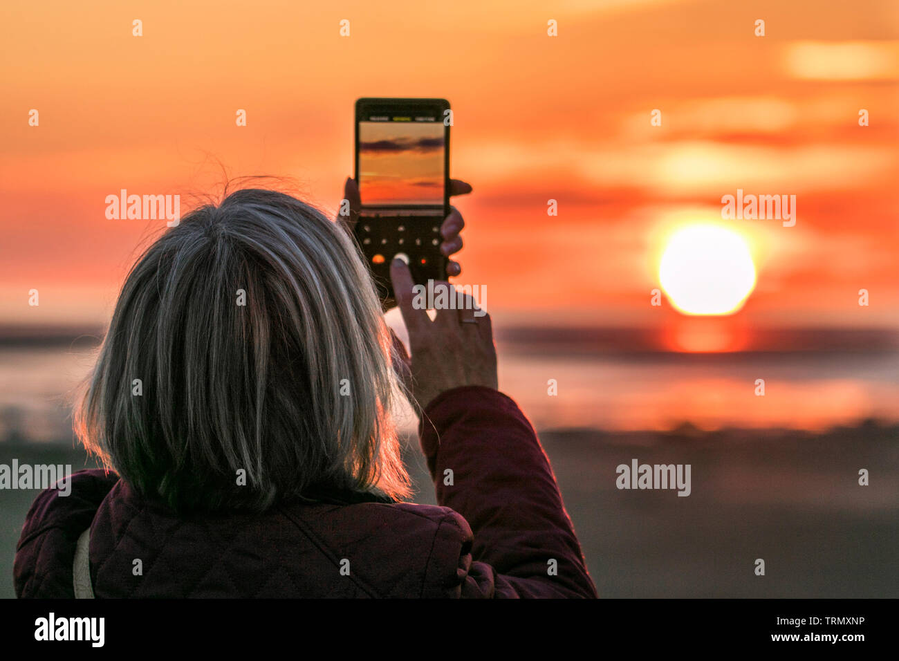Southport, Merseyside, UK. 9th June 2019.  A woman takes a picture of the beautiful sunset as it nestles into bed on the horizon at Southport in Merseyside.  Credit: Cernan Elias/Alamy Live News Stock Photo