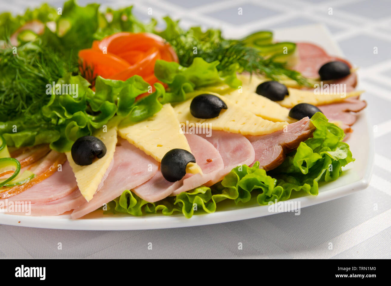 banquet cutting with ham, meat delicacies, cheese, sausage smoked, olive, lettuce and tomato on white dish. Stock Photo