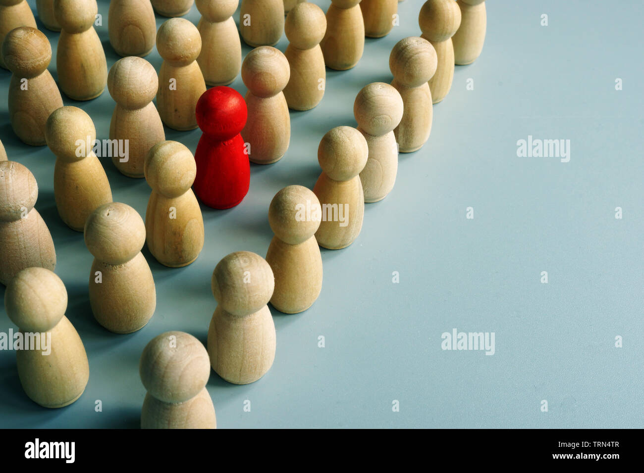 Unique red figurine stand out in the crowd from wooden ones. Stock Photo