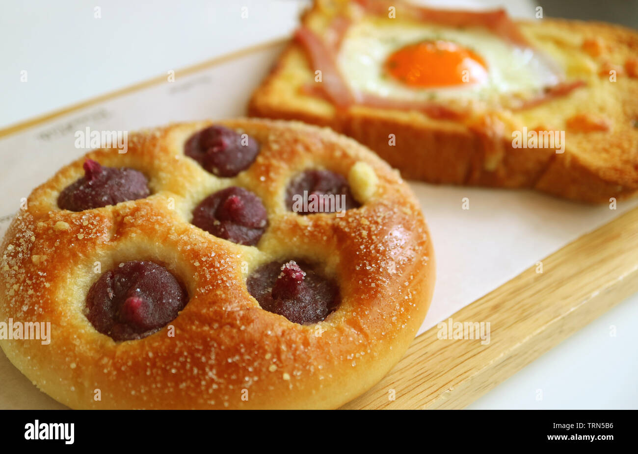Closeup purple sweet potato cream bun with blurry egg and ham toast in background Stock Photo