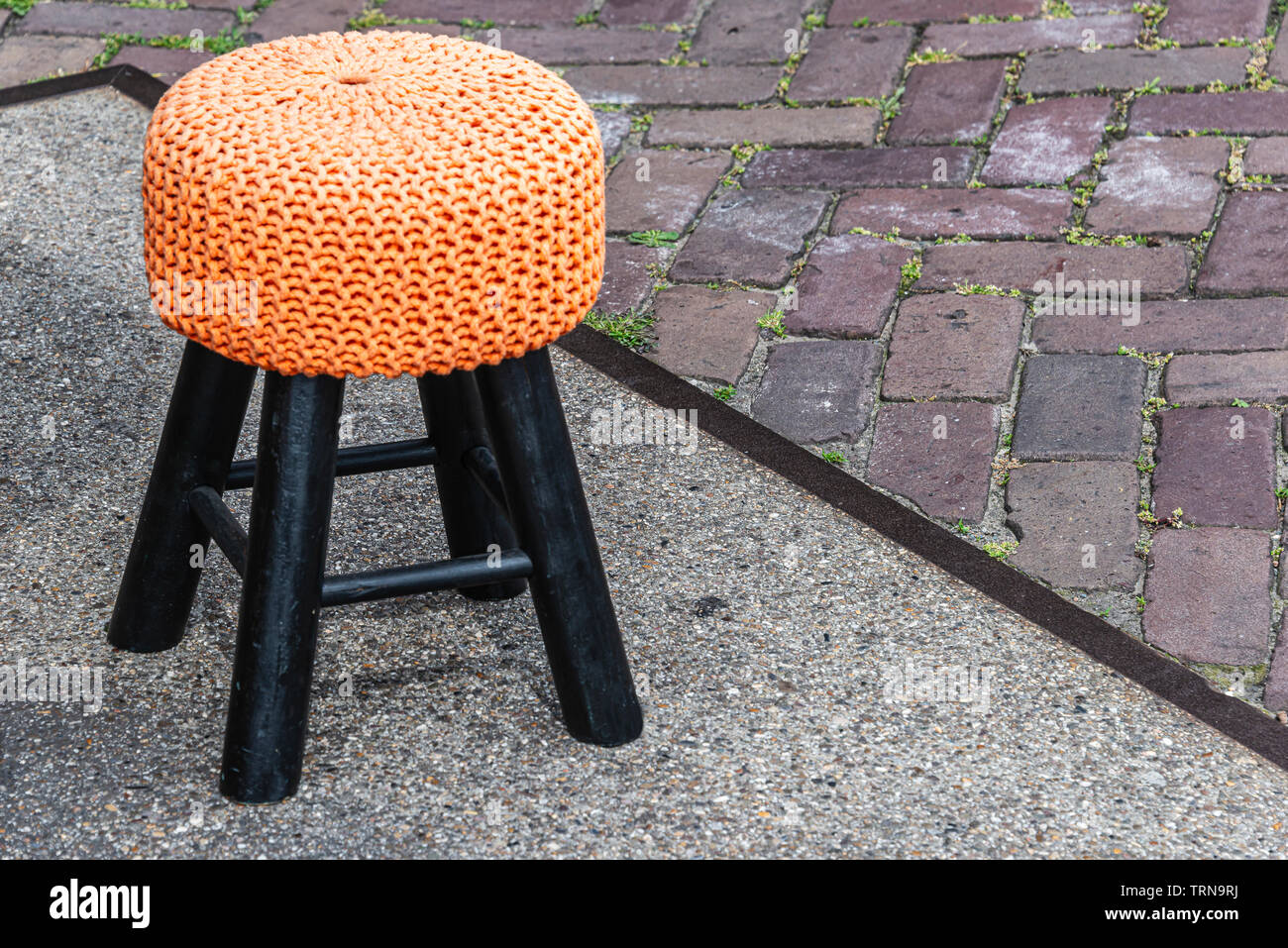little black stool with orange seat is on the street Stock Photo