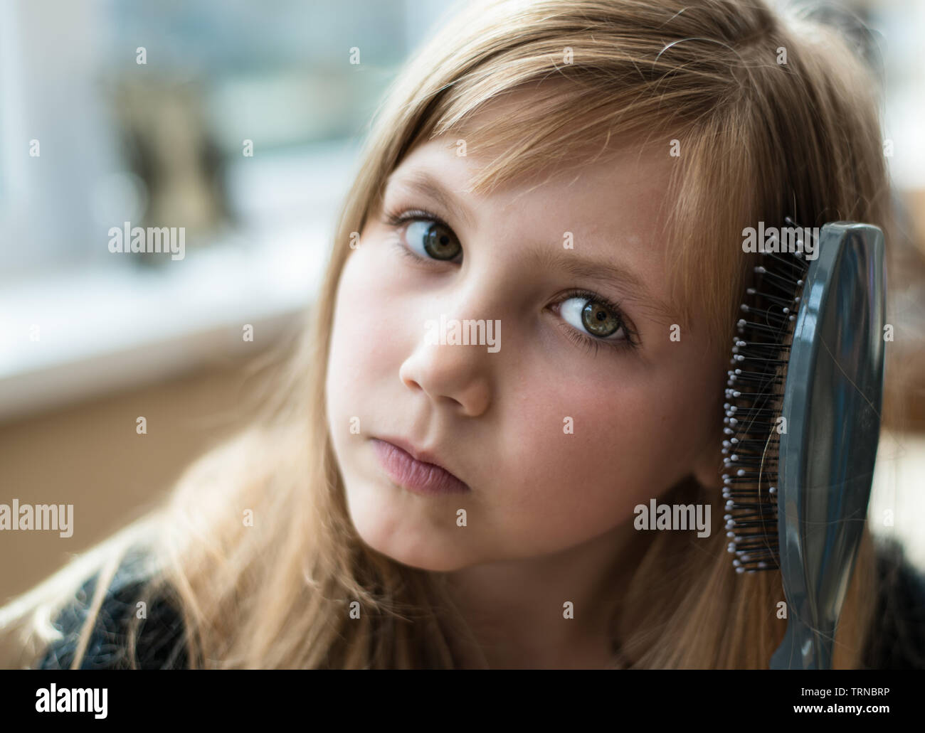 Pretty Young blonde girl brushing her hair and looking coy Stock Photo