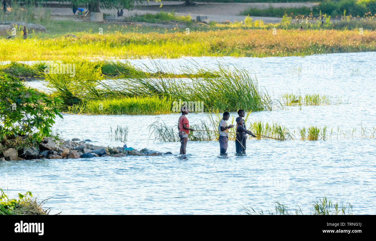 boys stand in Lake Malawi fishing with home made fishing rods Malawian boys stand in Lake Malawi fishing with home made fishing rods Stock Photo