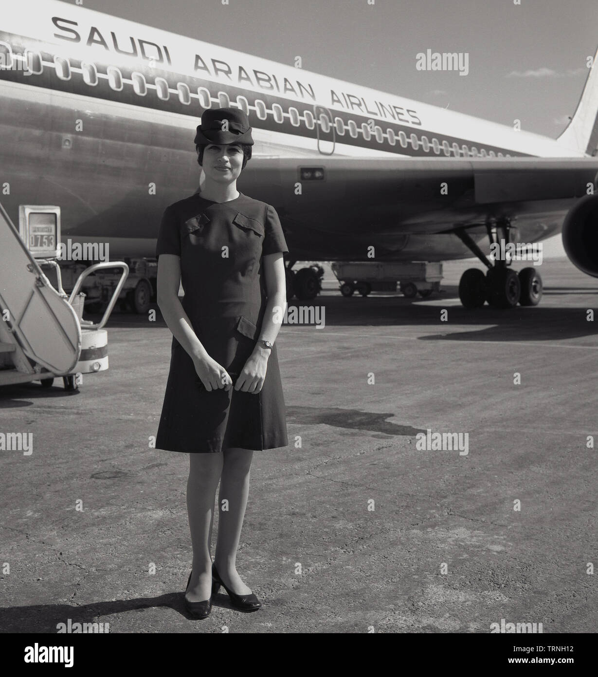 1960s, historical, Uniformed female Air hostess standing outside a Saudi Arabian Airlines jet aircraft, Heathrow airport, London, England, UK. Stock Photo