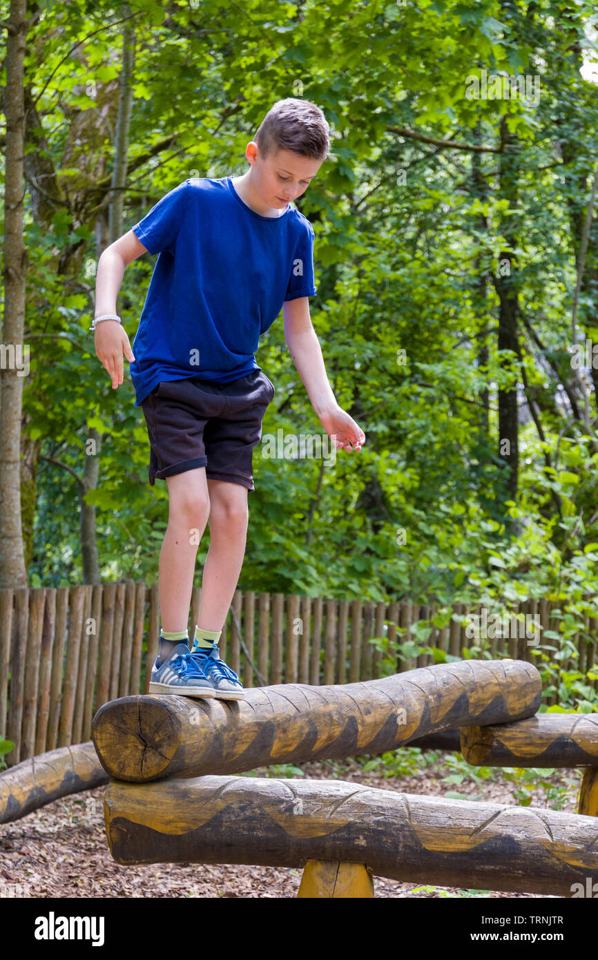 Young 11 year old caucasian boy outdoors in summer playing balancing on wooden snake at natural playground a play area constructed of sculpted wood Stock Photo