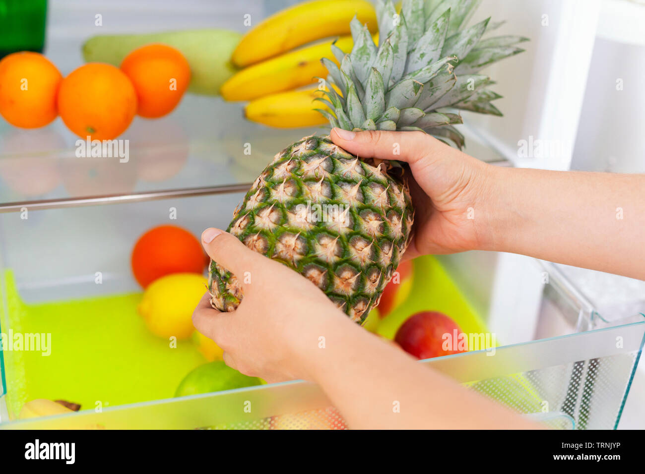 Woman getting a pineapple from fridge. Close up. Stock Photo