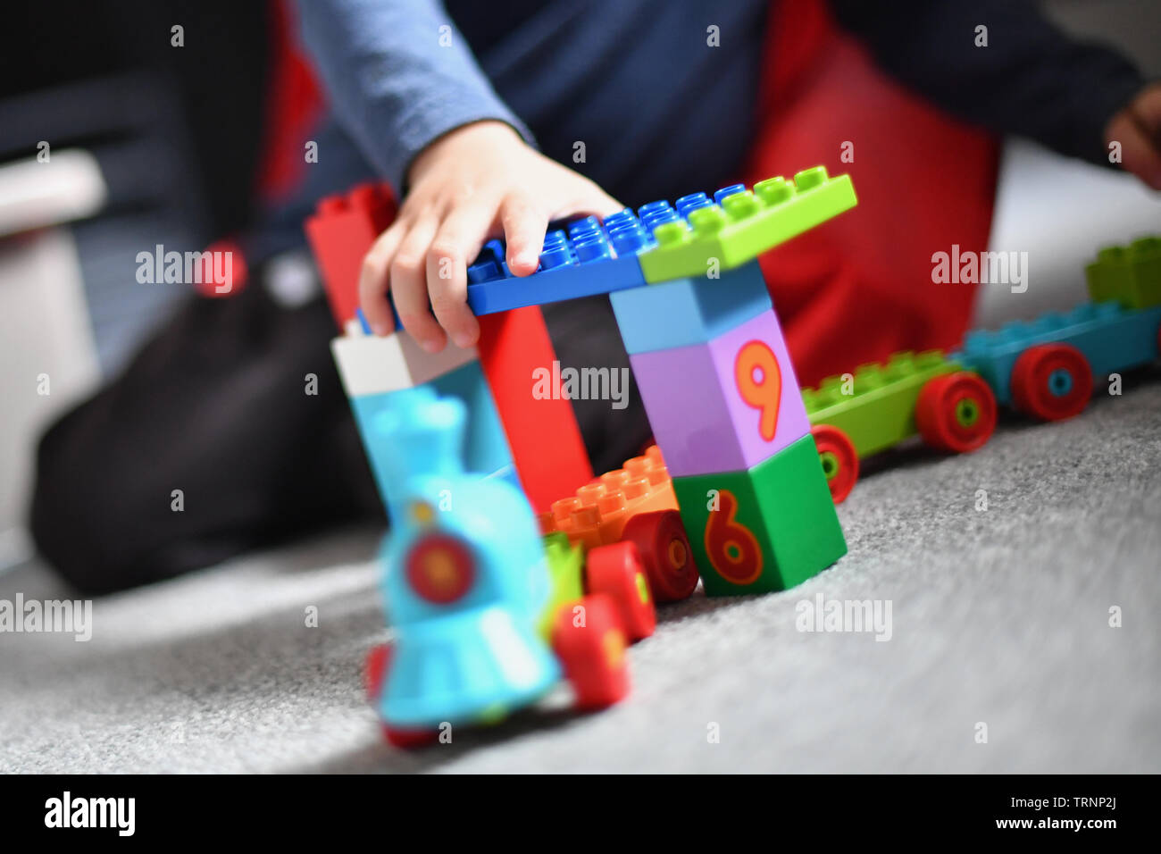 A boy dresses in a cap and mask plays with Lego Duplo blocks Stock Photo