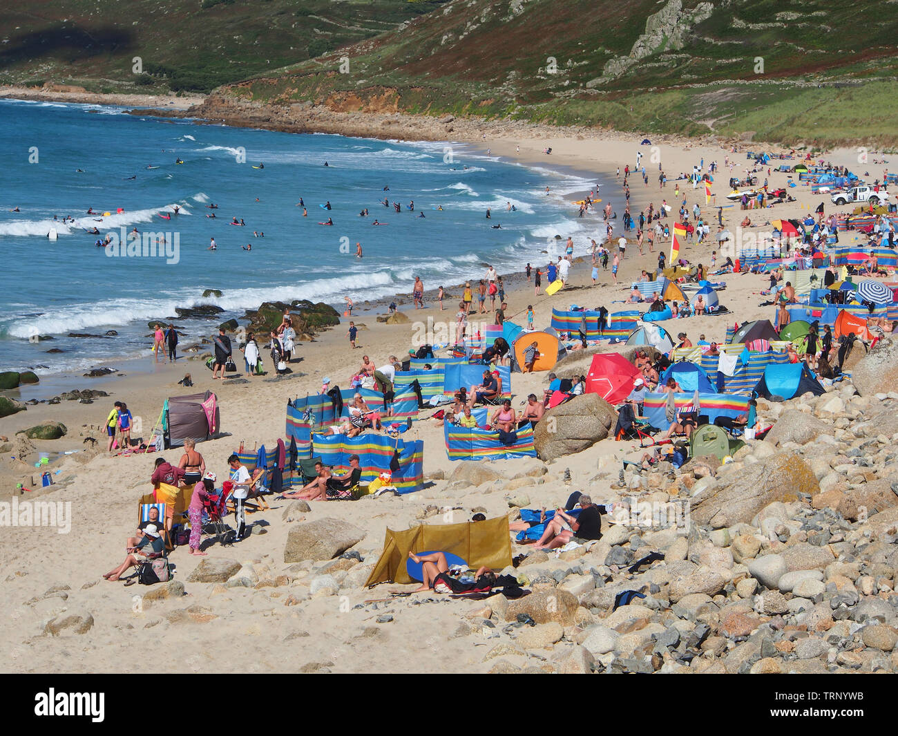 Crowds of people enjoying a sunny summers day on the beach in Sennen Cove, Cornwall, England UK showing the sandy beach and blue sea under a blue sky. Stock Photo