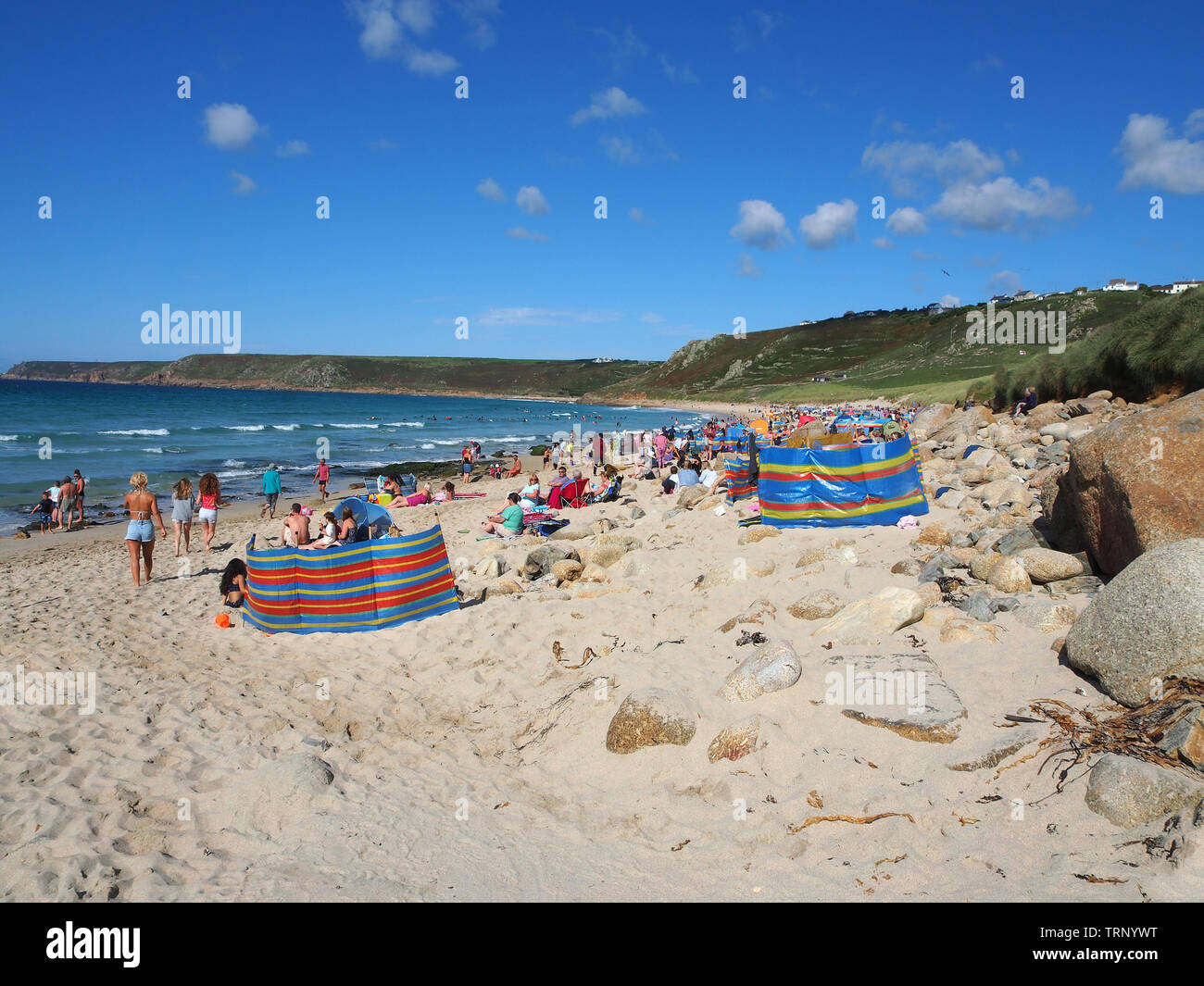 People enjoying sunny summers day on the beach in Sennen Cove, Cornwall, England, UK showing the sandy beach and blue sea under a blue sky. Stock Photo