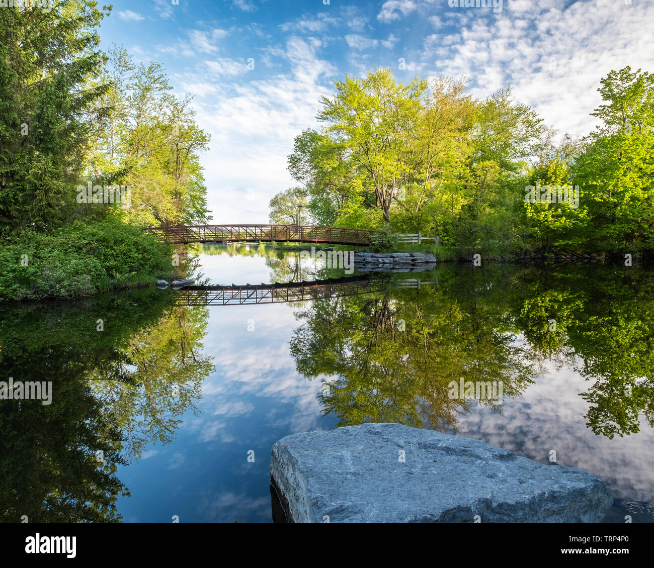 A beautiful spring morning shot of the Beavermead park footbridge and it’s reflection, over the perfectly still water of a branch of the Otonabee rive Stock Photo