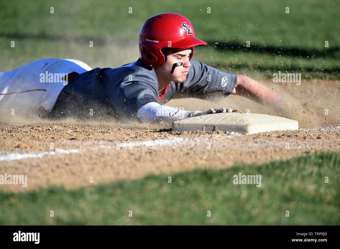 Base runner sliding head first safely into third base with a triple. USA. Stock Photo