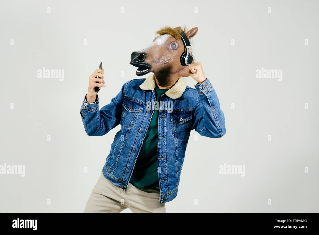Unrecognizable man disguised with a horse head using phone and listening music on headphones