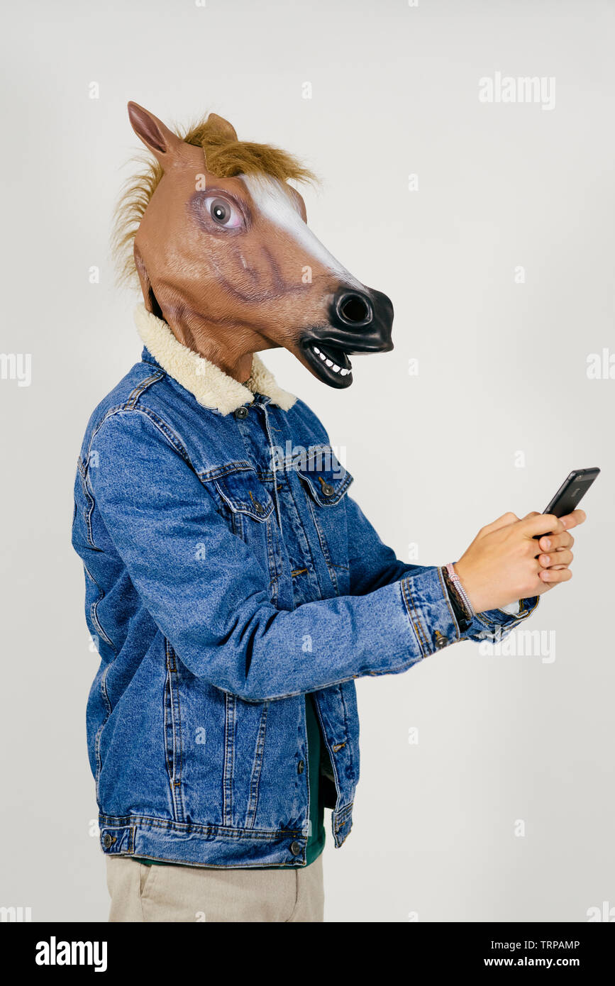 Unrecognizable man disguised with a horse head using phone and listening music on headphones