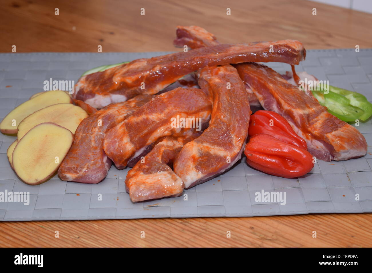 Marinated uncooked pork ribs laid on a clean grey surface with organic sliced vegetables Stock Photo