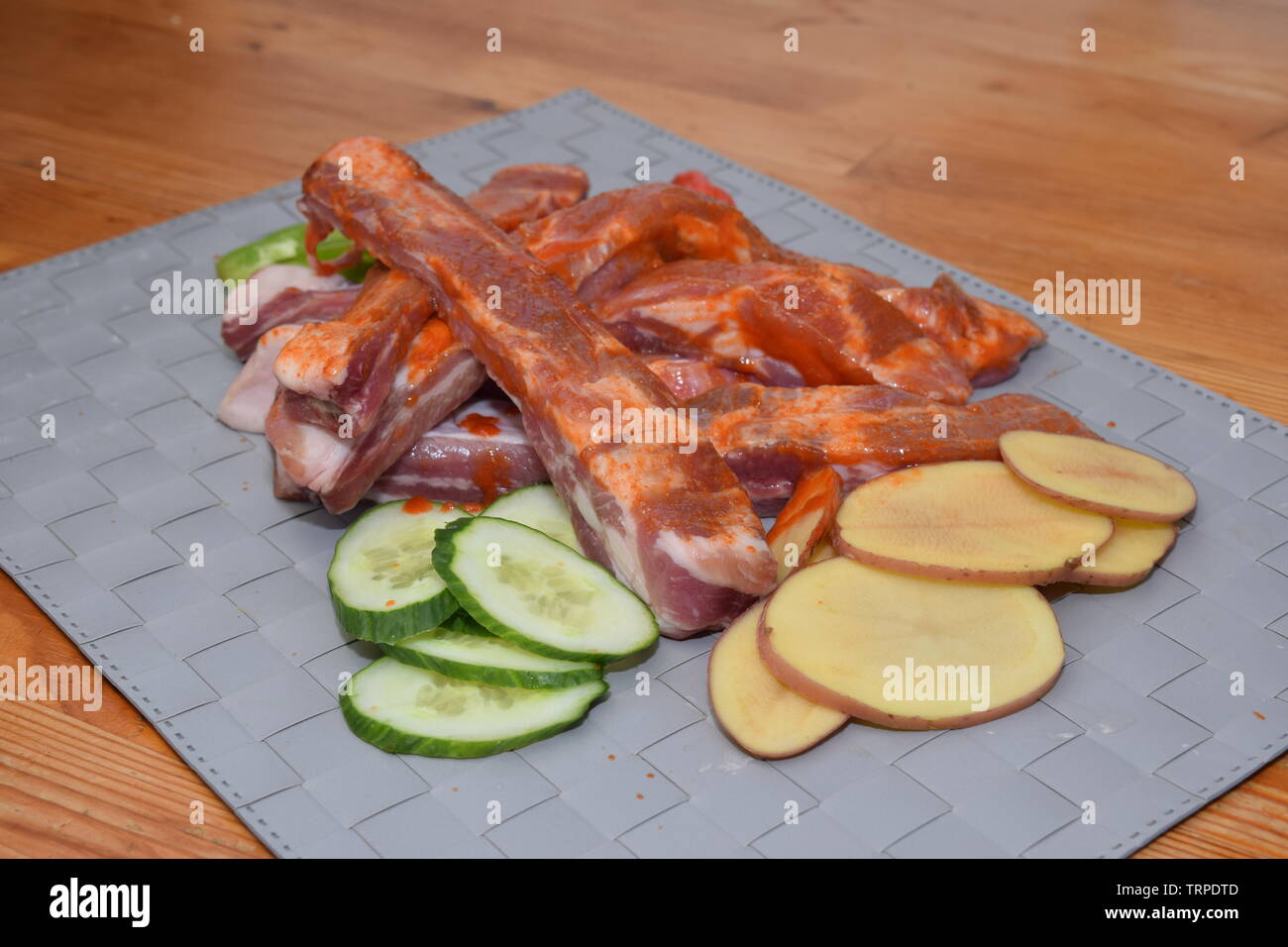 Marinated uncooked pork ribs laid on a clean grey surface with organic sliced vegetables Stock Photo